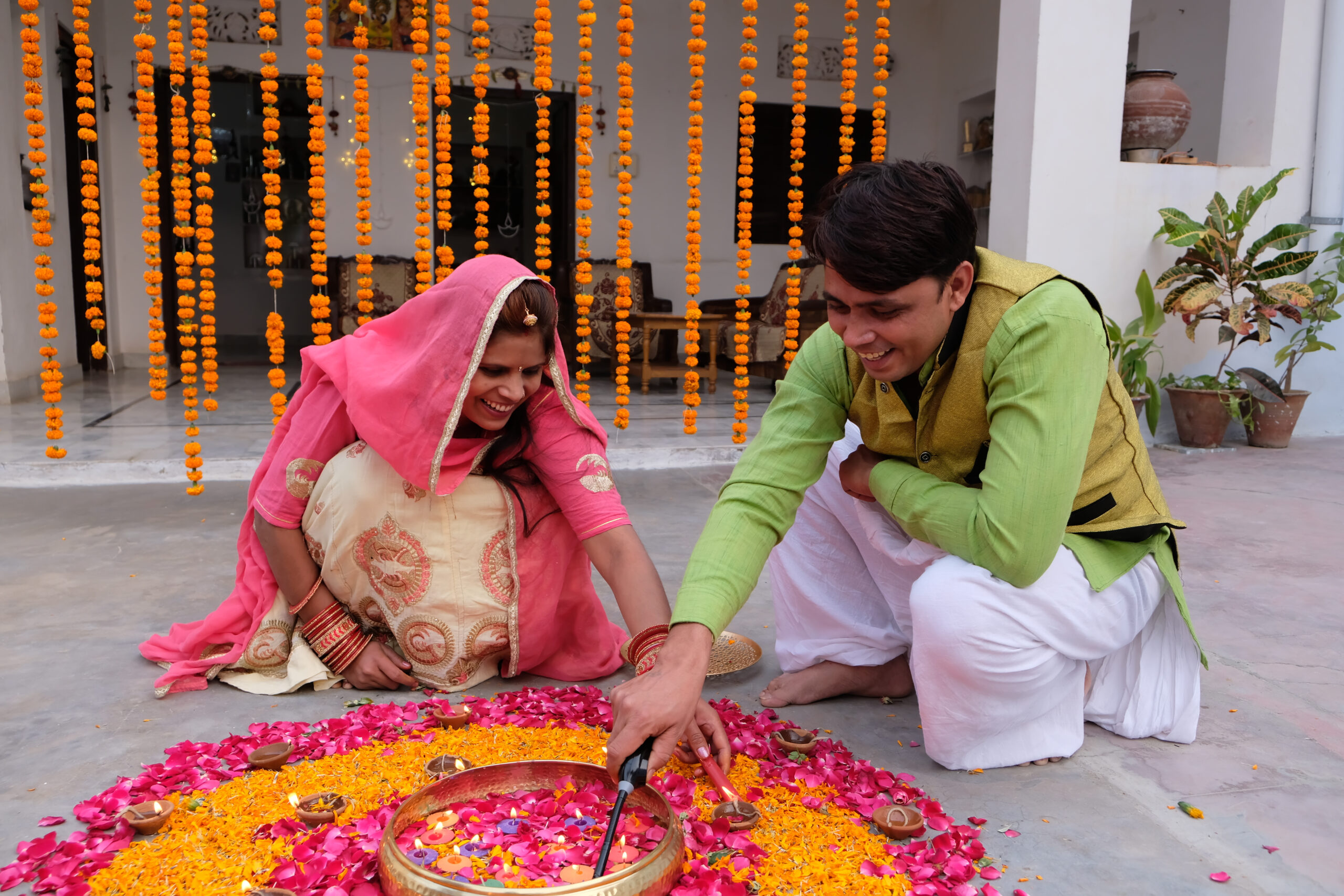The Indian family creating rangoli on the ground using candles, marigold and pink rose petals